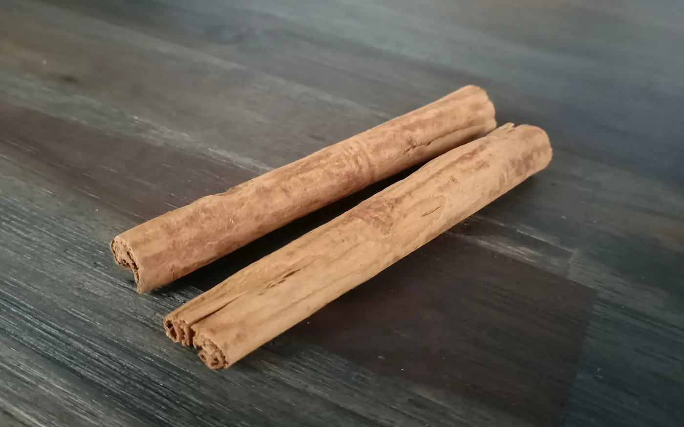 Two hand-rolled Ceylon cinnamon quills on a grey wooden bench, the layered rolls visible at the cut ends.