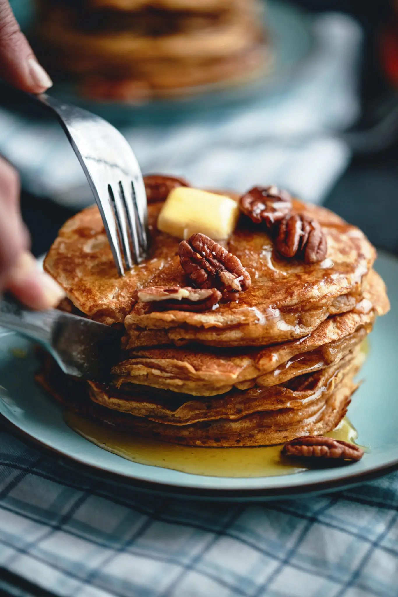A stack of cinnamon pancakes topped with butter and pecans, syrup pouring over