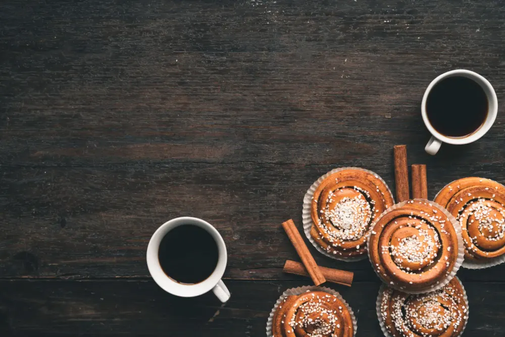 Cinnamon buns dusted with icing sugar around two cups of black coffee, seen from above