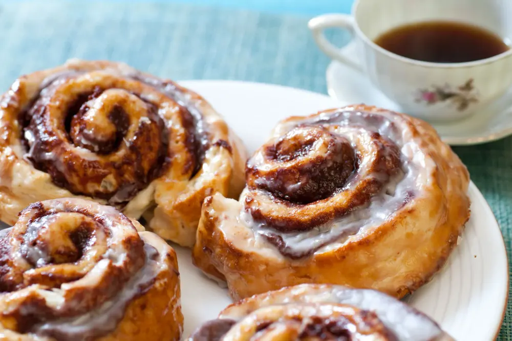 Iced cinnamon scrolls on a plate beside a cup of tea