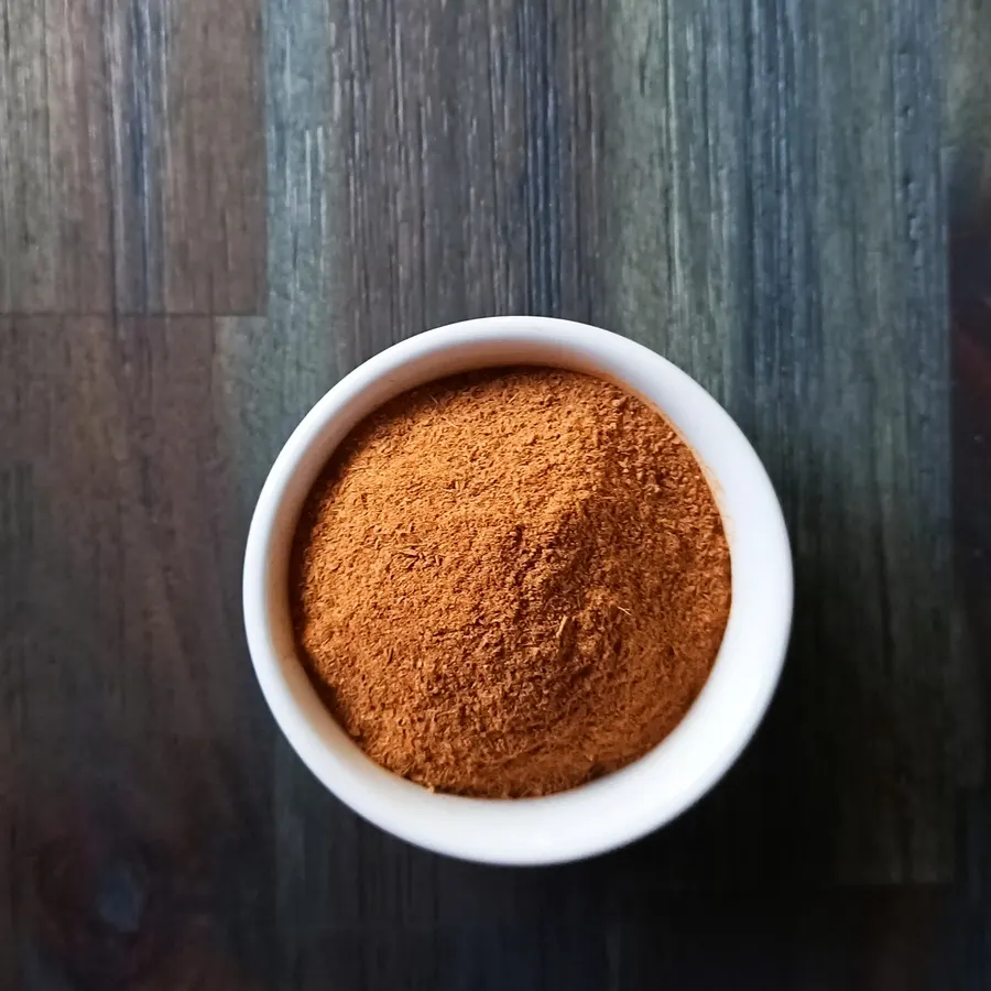 A white bowl of freshly ground Ceylon cinnamon on a dark wooden bench