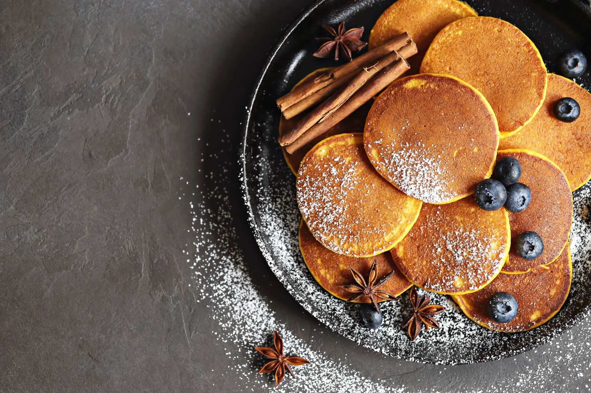 Small spiced pancakes in a pan with blueberries, cinnamon quills and star anise