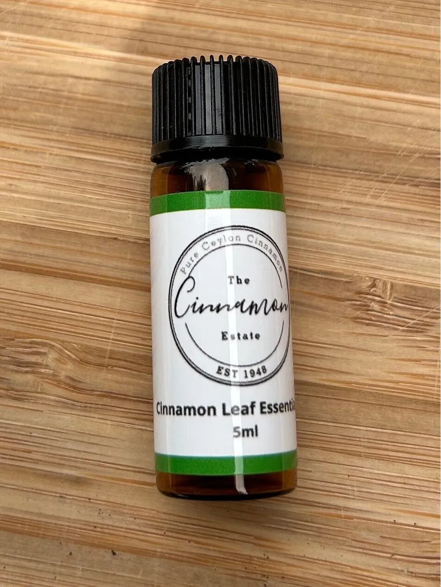 An amber dropper bottle of The Cinnamon Estate cinnamon leaf essential oil, with a green striped label, on a bamboo board.